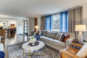 A modern living room with a sofa, coffee table, and lamps. A kitchen is visible in the background. - Charming Connecticut Hideaway: Year-Round Fun! (Middlefield)