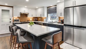 Cocina moderna con armarios blancos, un refrigerador de acero inoxidable grande y una isla central con taburetes de bar.