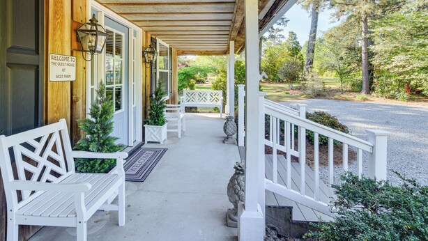 Un portico in legno con panchine bianche, un cartello di benvenuto e vista sul giardino circostante.