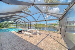 A covered outdoor area with a pool, lounge chairs, and a table. - Cape Villa w Heated Saltwater Pool-Private Dock-Gulf Access (Cape Coral)