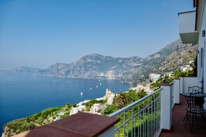Un balcon avec vue sur la mer et les montagnes, un bâtiment blanc et du mobilier d’extérieur.