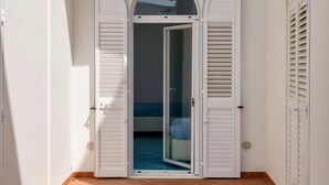 Ein Zimmer mit einer Glasschiebetür, weißen Läden und einem gefliesten Boden.
