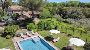 A swimming pool with lounge chairs and umbrellas, surrounded by a garden and a house with a tiled roof. - Mas Du Tilleul (Saint-Rémy-de-Provence)