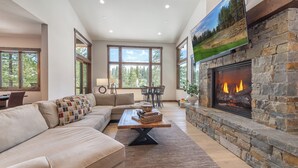 A living room with a stone fireplace, a sofa, a coffee table, and a television mounted on the wall. - Fairway Estate: Hot Tub, Fire Pit & Dog Friendly (Truckee)