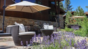 A patio area with wicker furniture, stone walls, and purple flowers. - Fairway Estate: Hot Tub, Fire Pit & Dog Friendly (Truckee)