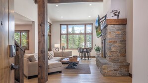 A spacious living room with a stone fireplace, a sofa, a coffee table, and a dining area with chairs. - Fairway Estate: Hot Tub, Fire Pit & Dog Friendly (Truckee)