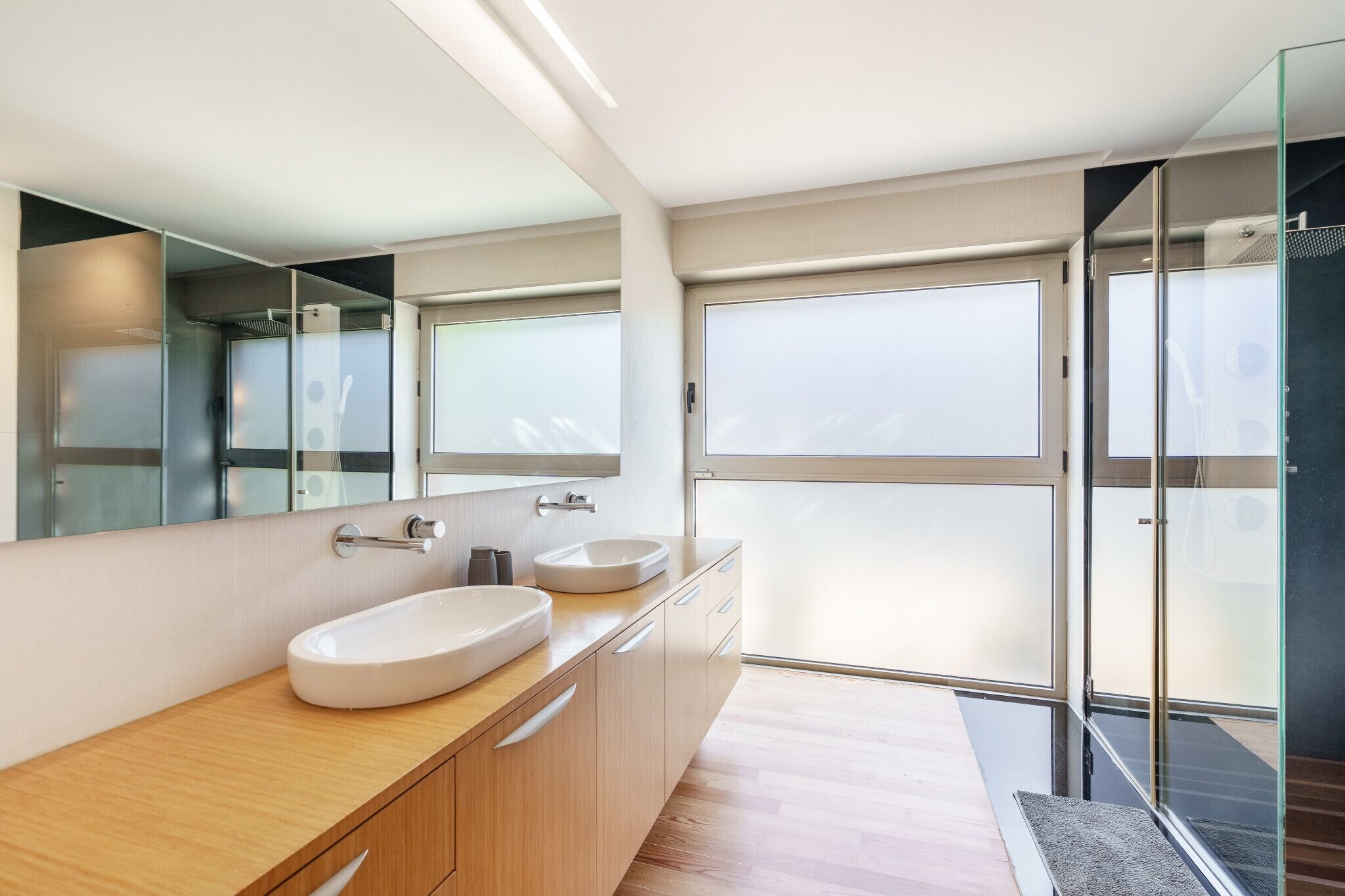 A modern bathroom with a large mirror, two sinks, and a glass shower enclosure.
