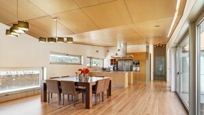 Eine geräumige Küche mit modernen Geräten, ein Essbereich mit Holztisch und -stühlen sowie große Fenster für natürliches Licht.