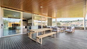 Eine großzügige Terrasse mit Holzboden, einem langen Tisch und einer Sitzecke mit Kissen.
