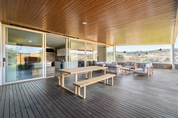A spacious deck with wooden flooring, a long table, and seating area with cushions. - The Ehrlich Essence Villa by Minho s Guest (Braga)