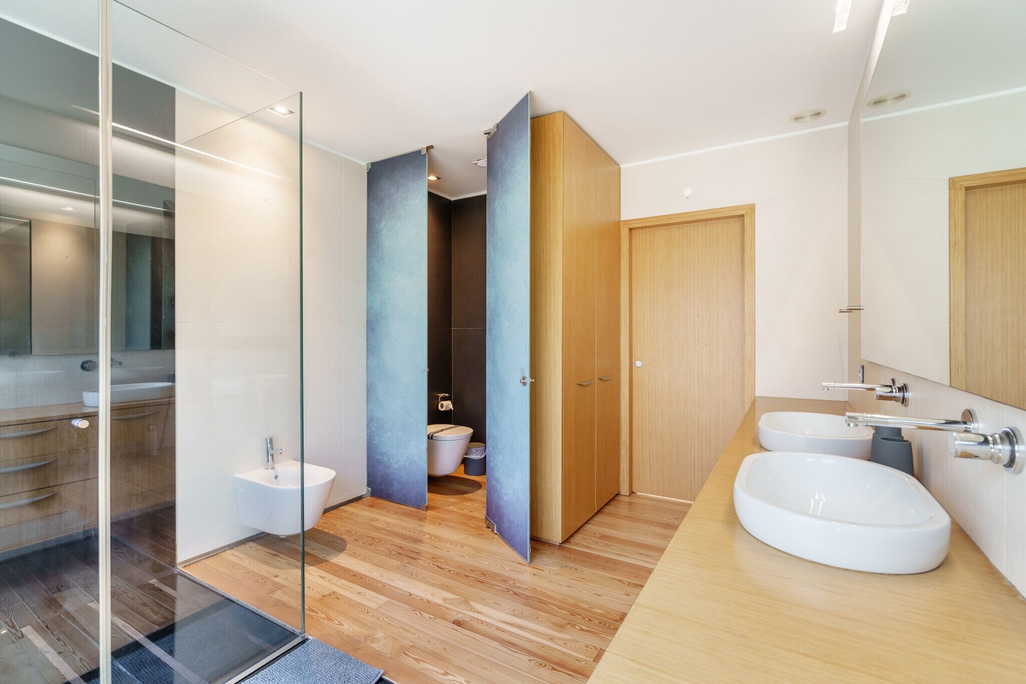 Une salle de bain moderne dotée d’une douche à parois de verre, d’un meuble-lavabo en bois et d’un espace toilettes séparé.