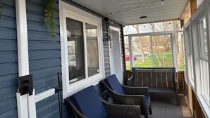 A covered porch with two wicker chairs, a hanging plant, and a view of a residential street. - Hot Tub Retreat Near Downtown & Casino | Sleeps 8 | Cozy Luxury Stay for family✨ (Windsor)