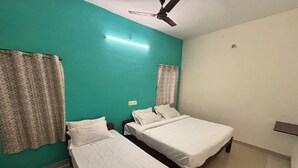 A room with two single beds, a ceiling fan, and a wall-mounted light fixture. - Thamira Residency (Yercaud)