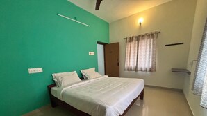 A bedroom with a bed, a green wall, a door, and a window with curtains. - Thamira Residency (Yercaud)