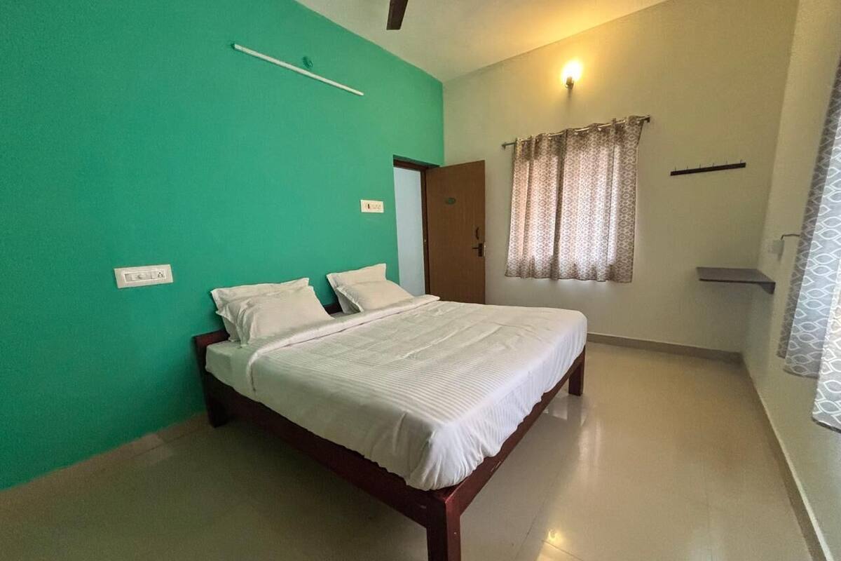 Un dormitorio con cama, pared verde, puerta y ventana con cortinas.