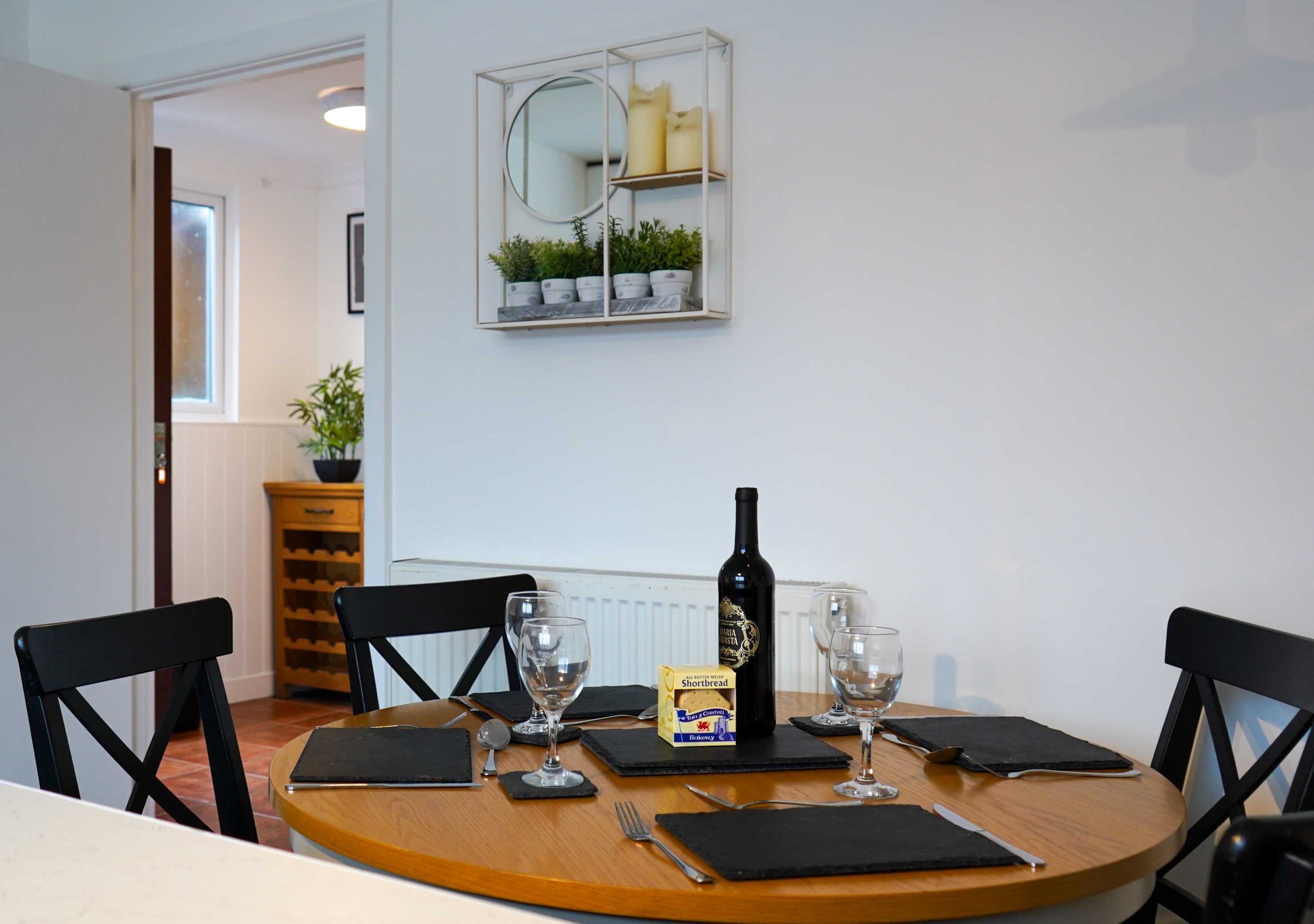 A dining table with four chairs, a wine bottle, and a box of bread.