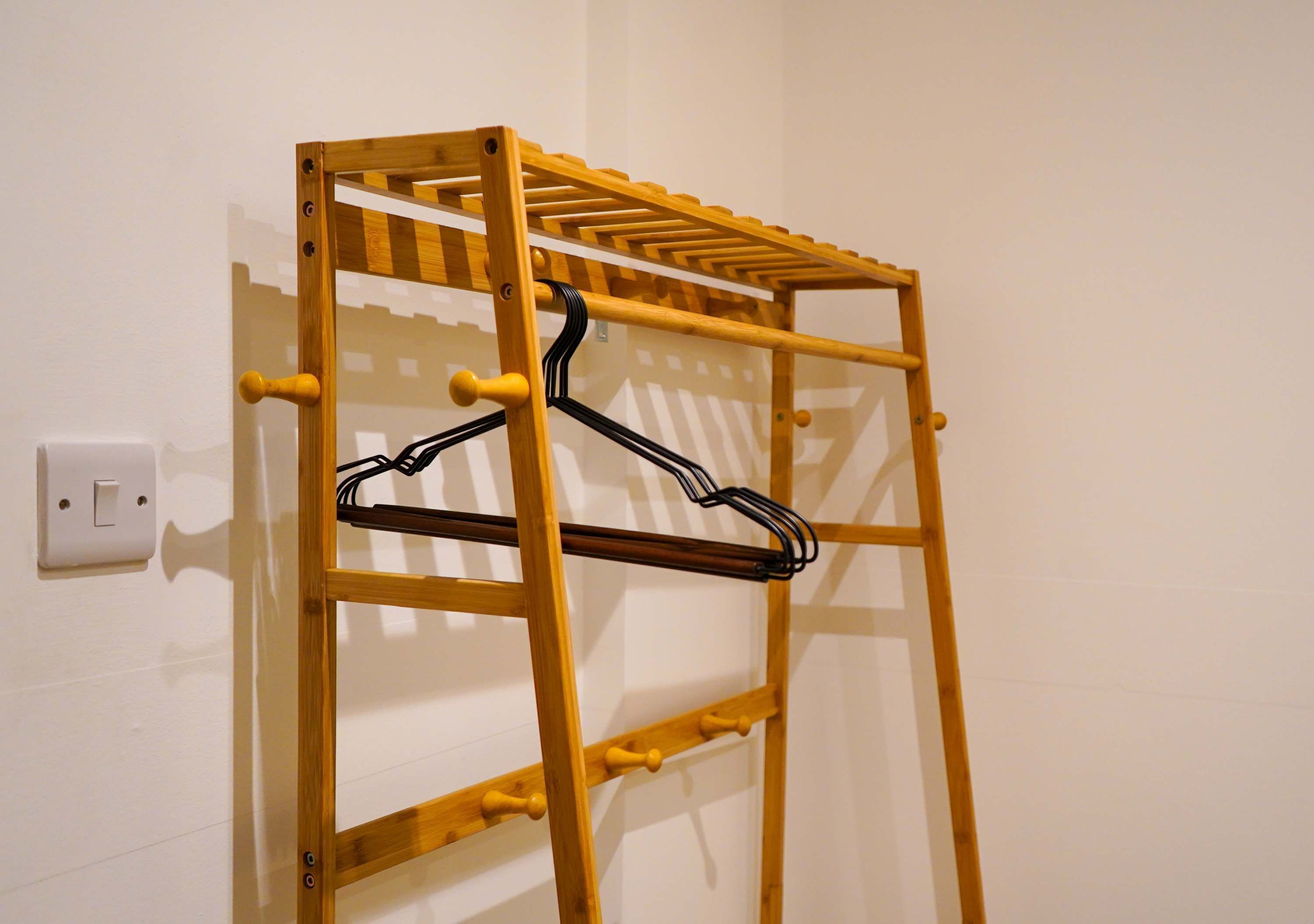 A wooden drying rack with multiple hooks and a shelf, mounted on a white wall.