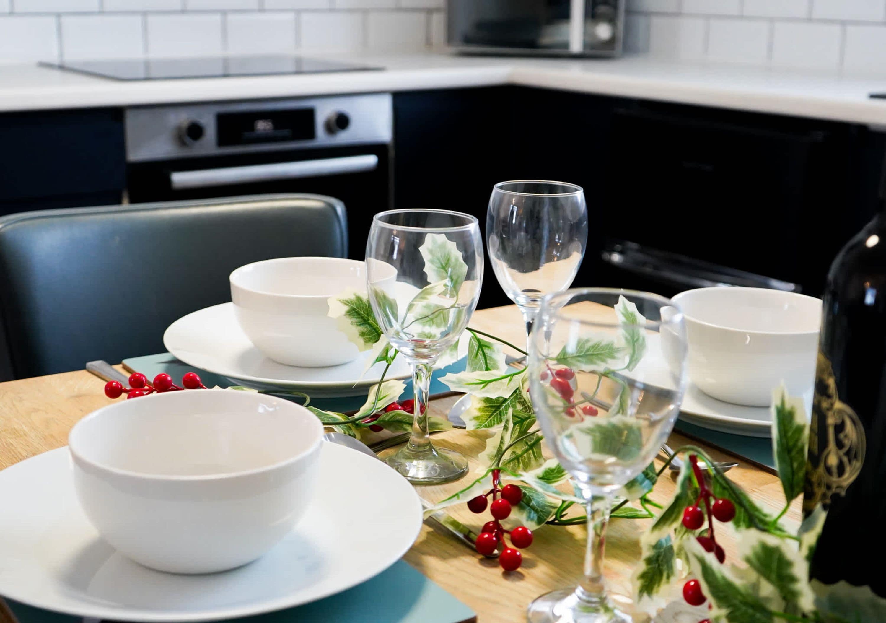 A dining table set with white bowls and wine glasses, decorated with holly and berries.