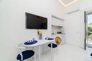 A compact kitchen with white cabinets, a flat-screen TV, a dining table with chairs, and a small refrigerator. - Casa Giulia Positano (Positano)