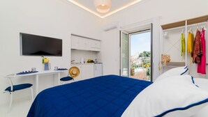 Quarto com cama, escrivaninha, televisão e varanda com roupas.