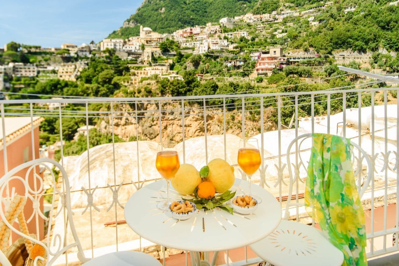 Un balcón con una mesa dispuesta para dos, con vistas a un pueblo en la ladera.