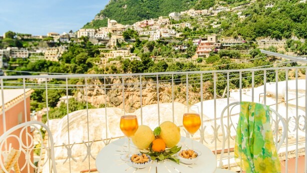 Varanda com mesa posta para dois, com vista para uma vila na encosta.