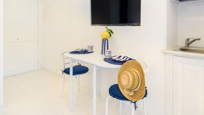 Um quarto branco com televisão, uma mesa com cadeiras, um chapéu e frutas.