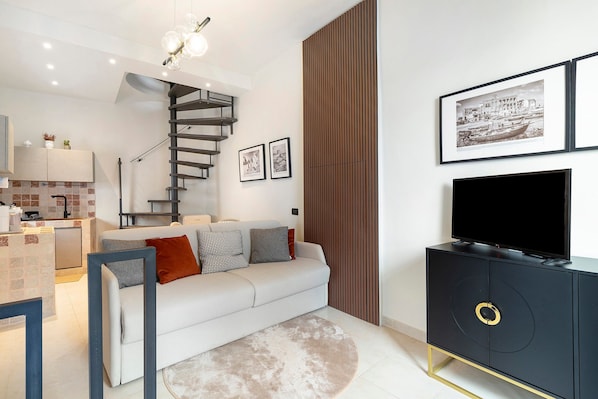 Ein modernes Wohnzimmer mit einer Couch, einem Fernseher, einer Treppe und gerahmten Bildern an der Wand.