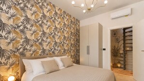 Een slaapkamer met een bed, een garderobe, een trap en een muur met een tropisch bladpatroon.