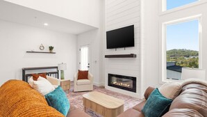 Ein modernes Wohnzimmer mit Kamin, Flachbildfernseher und Blick ins Freie.