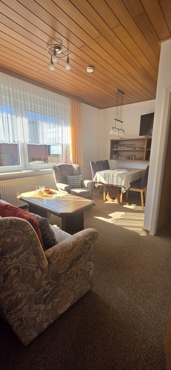 Un salon comprenant un canapé, une table basse, une table à manger avec des chaises, une bibliothèque et un téléviseur.