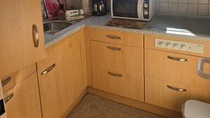 Cocina compacta con armarios de madera, microondas, cafetera y ventana con vistas.
