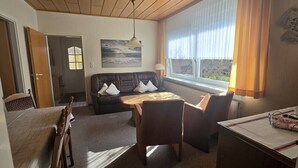 A room with a bed, a sofa, a dining table, and a window with curtains. - Vacation apartment 4 "Borkum" (Borkum)