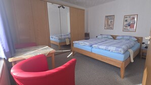 A bedroom with a bed, a red chair, a table, and two wall-mounted pictures. - Vacation apartment 4 "Borkum" (Borkum)