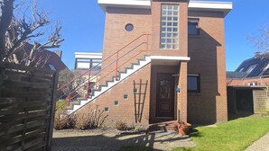 Un bâtiment en briques de deux étages, avec un escalier menant à l’entrée, un petit jardin et un garage.
