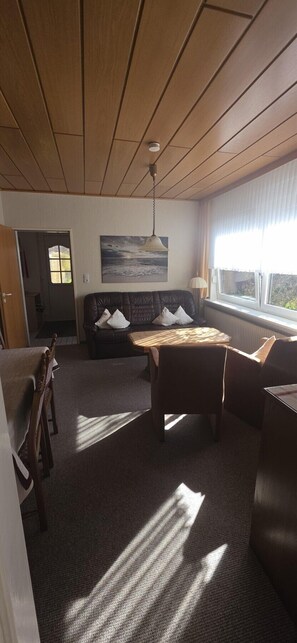 Una habitación con techo de madera, un sofá con cojines, una mesa, una lámpara y una ventana con cortinas.