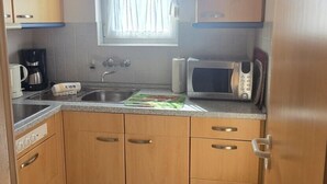 A compact kitchen with wooden cabinets, a microwave, a coffee maker, and a window with a curtain. - Vacation apartment 4 "Borkum" (Borkum)
