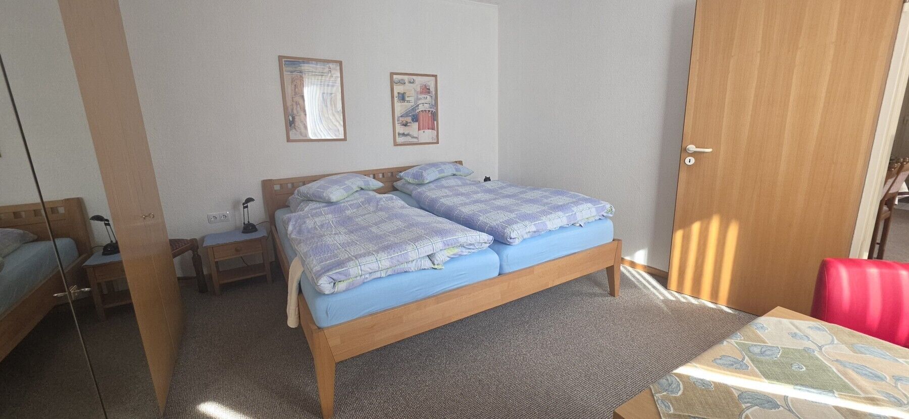 A bedroom with a wooden bed, a bedside table, a chair, and a door.