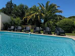 Une piscine à l’eau claire, entourée de chaises longues noires et de palmiers.