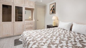 Een slaapkamer met een bed, nachtkastje, lamp, dressoir en een deur.