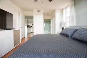 A bedroom with a bed, a TV, a desk, and a bathroom visible through an open door. - Amazing 2-bedroom apartment with AC in vibrant Miami (Miami)