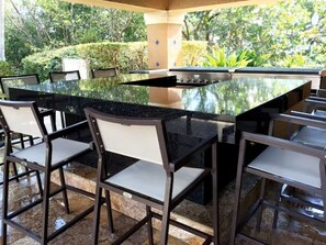 An outdoor bar area with a large island, bar stools, and a view of the surrounding greenery. - Amazing 2-bedroom apartment with AC in vibrant Miami (Miami)