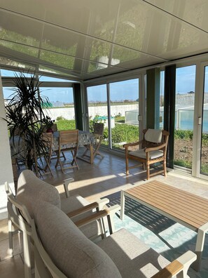 Ein sonnendurchfluteter Raum mit einer Couch, Sesseln, einem Tisch und großen Fenstern mit Blick auf Grünflächen und eine ferne Landschaft.