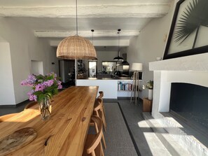 A dining area with a wooden table, chairs, a hanging light fixture, and a fireplace. - Charming village house with garden (Rognes)