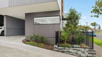 A modern building with a garage, a covered driveway, and a small garden area with a metal fence.