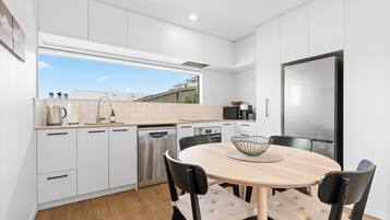 A modern kitchen with white cabinetry, a stainless steel refrigerator, and a dining area with a round table and four chairs.