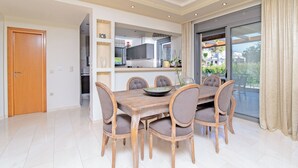 Een eethoek met een houten tafel en stoelen, een keuken op de achtergrond en een glazen schuifdeur naar buiten.