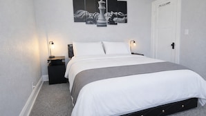 A neatly arranged bedroom with a bed, bedside tables, a wall-mounted artwork, and a door. - Modern Duplex Near Airport & Downtown + Game Room & Lake (Milwaukee)