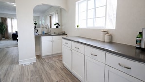 A modern kitchen with white cabinetry, a large window, and a view into the living area. - Modern Duplex Near Airport & Downtown + Game Room & Lake (Milwaukee)