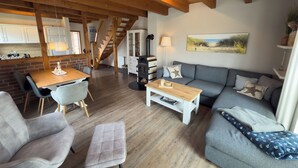 Una sala de estar acogedora con techo de madera, un sofá, una mesa de centro y una mesa de comedor con sillas.